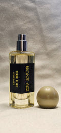 Perfume bottle labelled "Bronze age"
 with a spherical cap on a textured gray background 