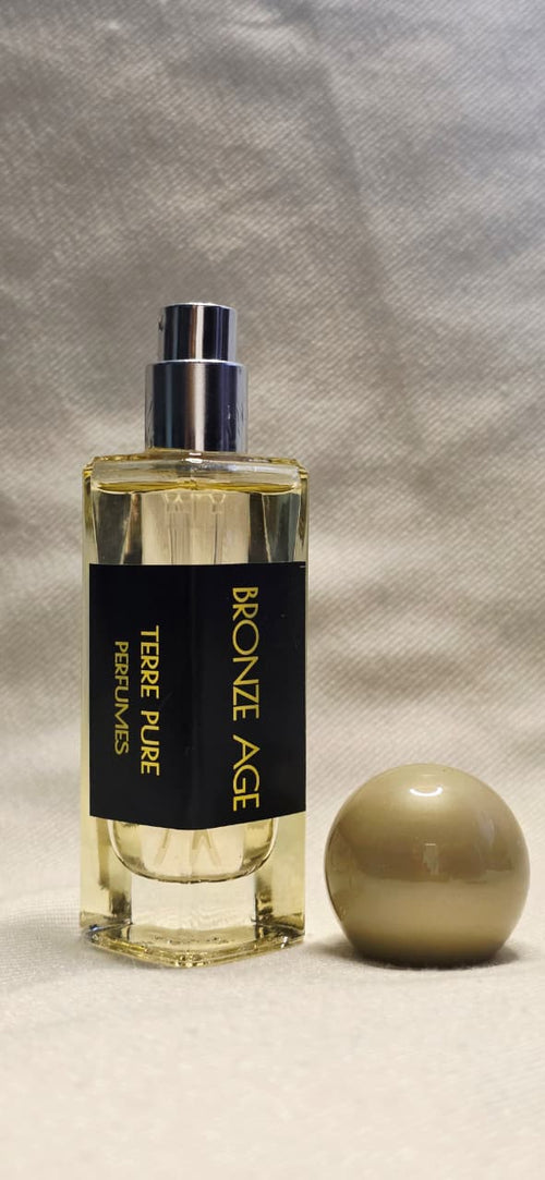 Perfume bottle labelled "Bronze age"
 with a spherical cap on a textured gray background 