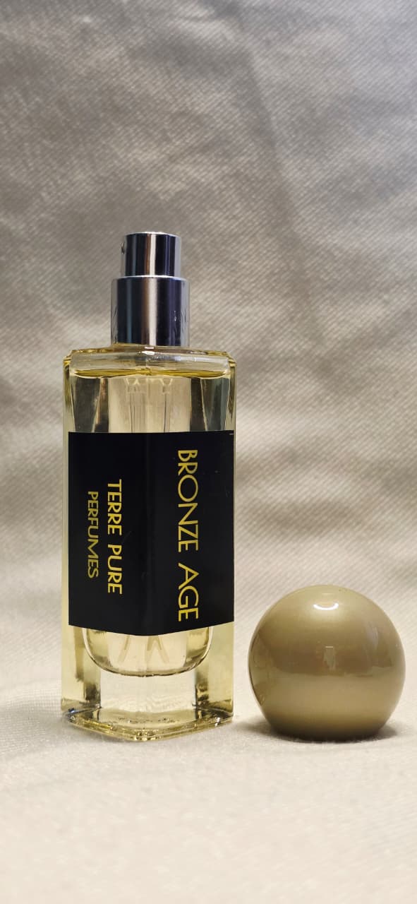 Perfume bottle labelled "Bronze age"
 with a spherical cap on a textured gray background 