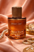 Brown Oud Terre Pure Indus perfume bottle on a pink fabric background with jewelry.