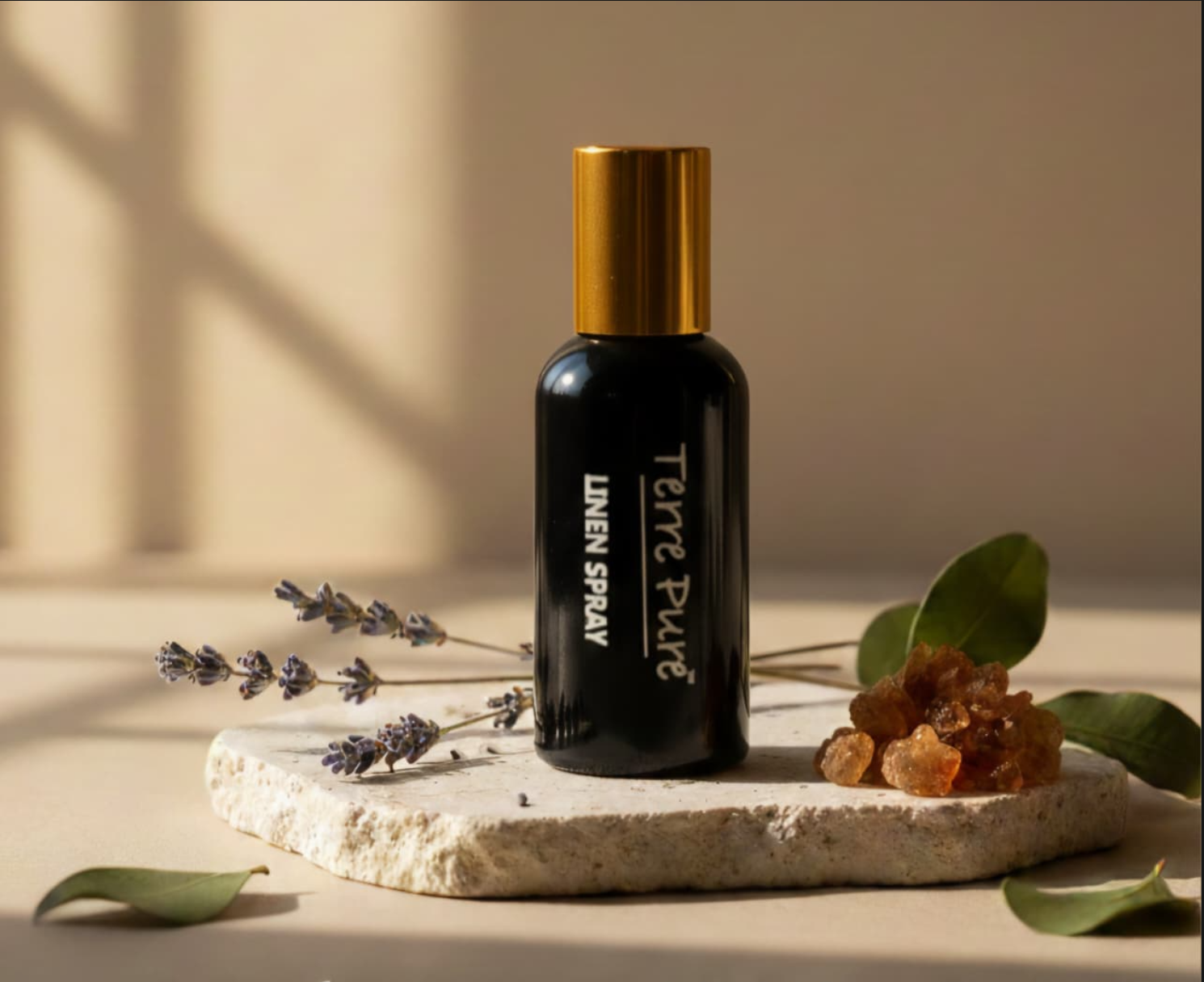 Black Linen Spray bottle with gold cap on a stone surface with lavender and leaves.