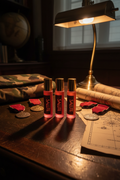 Four pink Perfume bottles labeled 'SALUTE' on a wooden surface with a lamp and documents in the background.